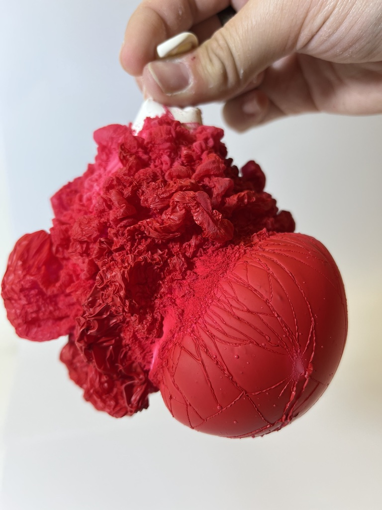 a hand holds a bunched up white balloon covered in fluffy-looking red clusters