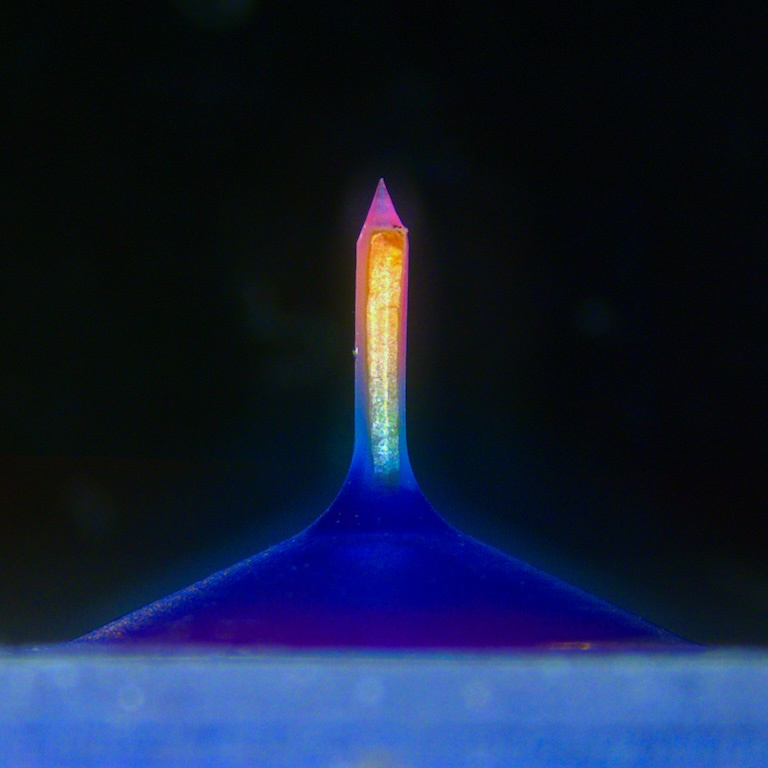 A glowing column with a gradient of pink to yellow to cyan mounted on a triangular indigo base