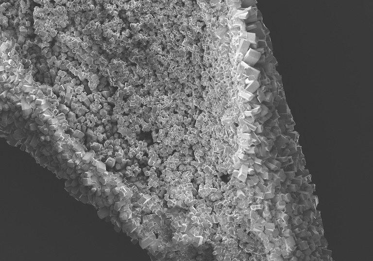 Black and white image of a pile of small square crystals, placed diagonally with a black background. The crystallization looks like a geode in form.